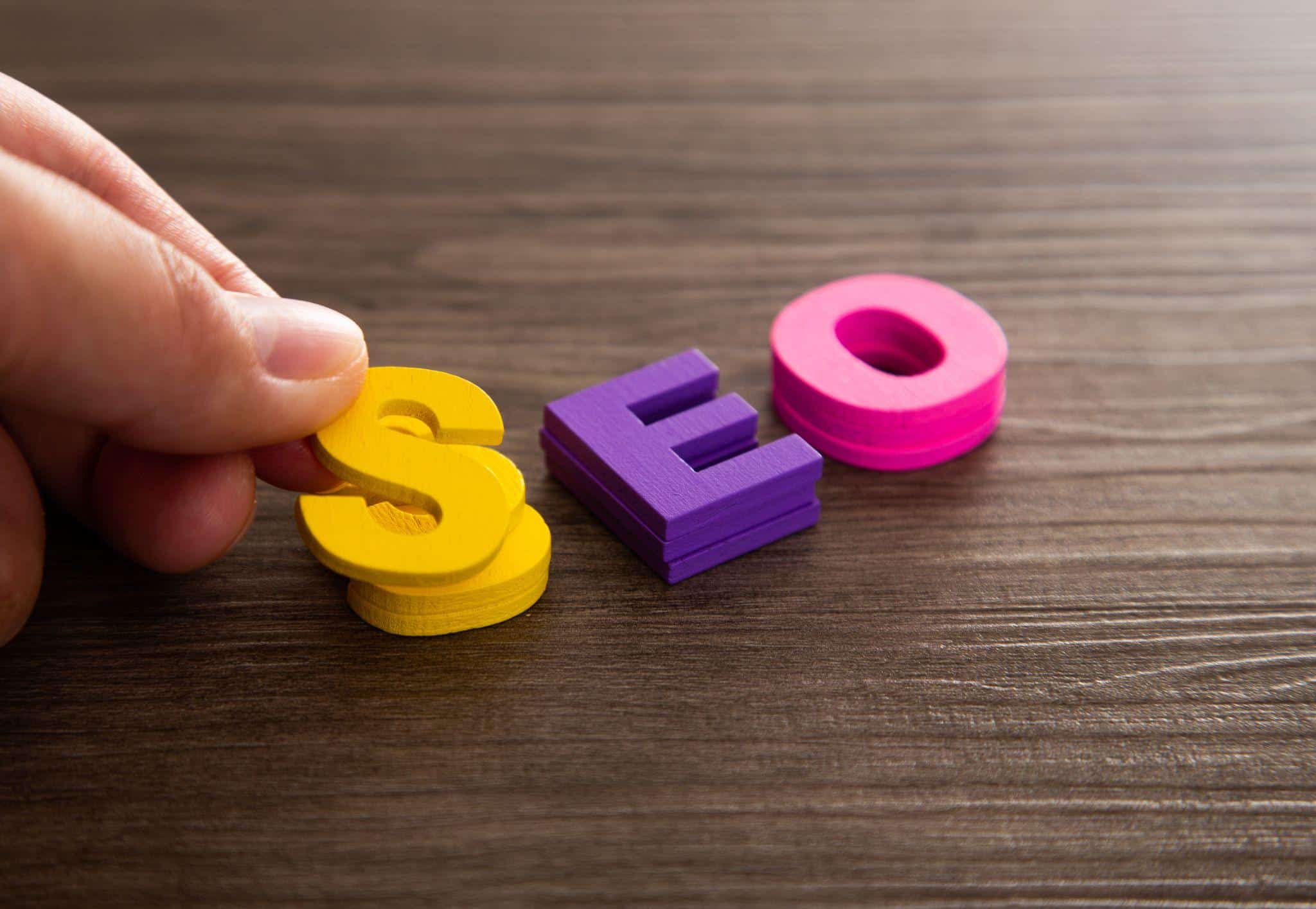 Hand placing colorful SEO letters on a wooden surface
